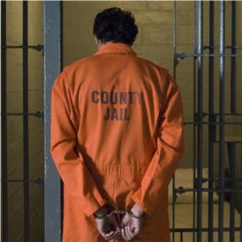 ClayCoNews stock image - Handcuffed criminal wearing prison uniform stands in jail